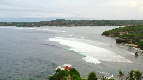 Costa-De-La-Isla-De-Nusa-Ceningan-Con-Olas-Y-Surfistas-En-El-Agua,-Antena