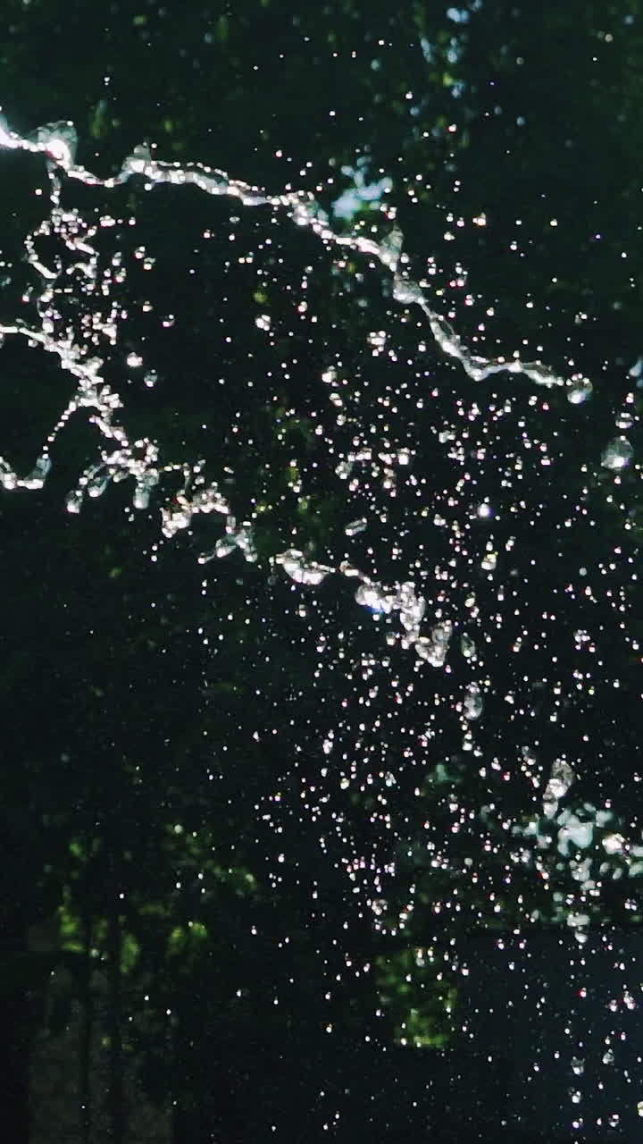 human's hands are holding a hose with water in the yard. Water are flowing by stream on the background of garden. Slow motion Vertical video
