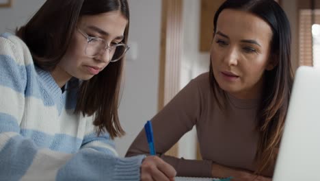 madre caucásica ayudando a su hija adolescente a hacer la tarea en la computadora portátil