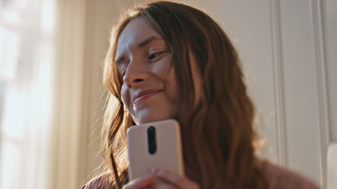 Nahaufnahme: Glückliches Mädchen hält Mobiltelefon im goldenen Sonnenlicht. Verliebter Teenager.