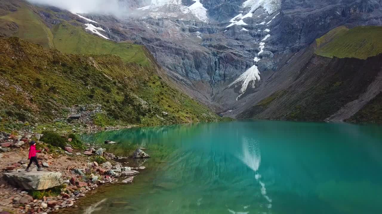 페루 쿠스코 지역 안데스 산맥 휴먼타이 호수의 바위 해안에서 하이킹을 하는 여성을 따라 공중, 드론 샷