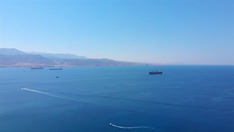 aerial view of cargo ships and speedboats in a calm sea with mountains