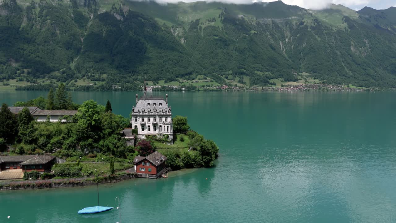 Close aerial orbit arround castle Seeburg revealing the view of the turquoise lake Brienzersee Iseltwald surrounded by the alpmointains on a sunny summer day in Switzerland near Interlaken