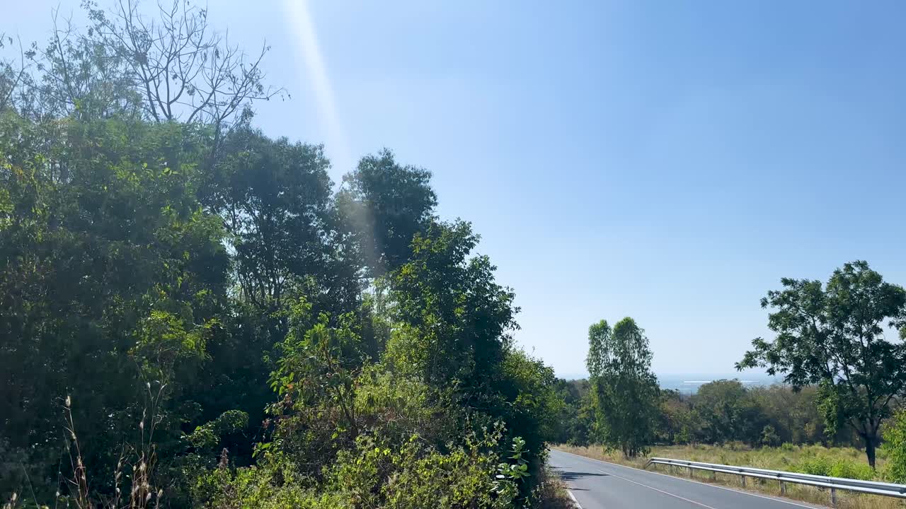 Point-of-view drive along sunny curved countryside asphalt road, surrounded by green forested hills