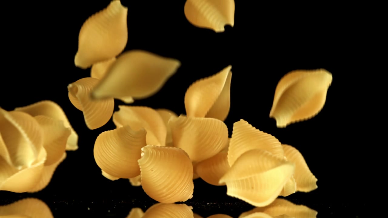 Golden Conchiglie Pasta Falling and Bouncing on Black Surface