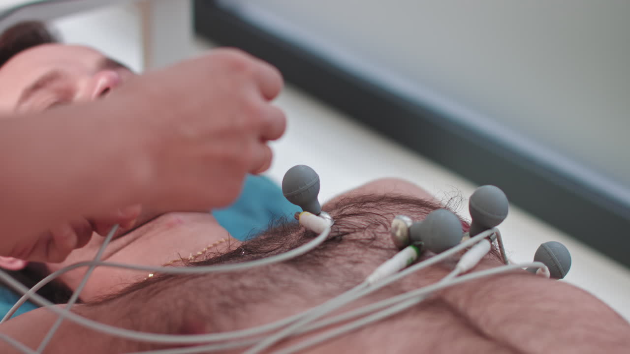 Krankenpfleger im Krankenhaus befestigt Elektroden an den Gliedmaßen eines Patienten für kardiologische Testgeräte, während sich der Arzt vorbereitet