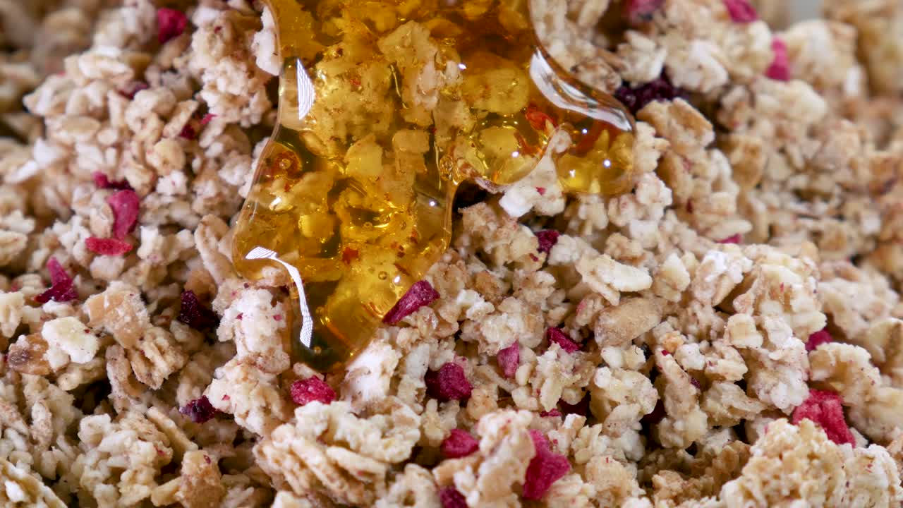 황금빛 액체 꿀이 과일과 함께 유기농 바삭한 뮤즐리 위로 천천히 흐릅니다.