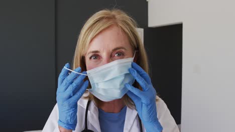 caucasian senior female doctor wearing surgical gloves putting on face mask