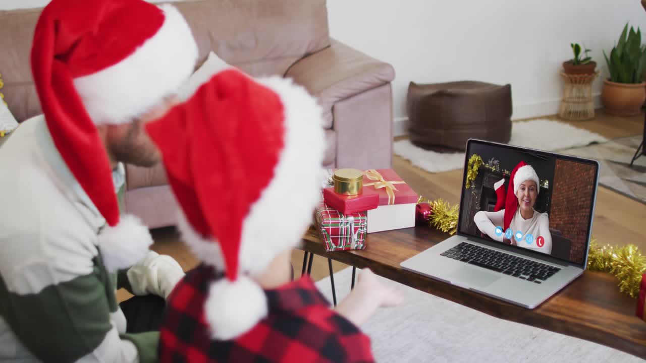 padre y hijo caucásicos usando sombreros de santa en una videochat portátil durante la navidad en casa