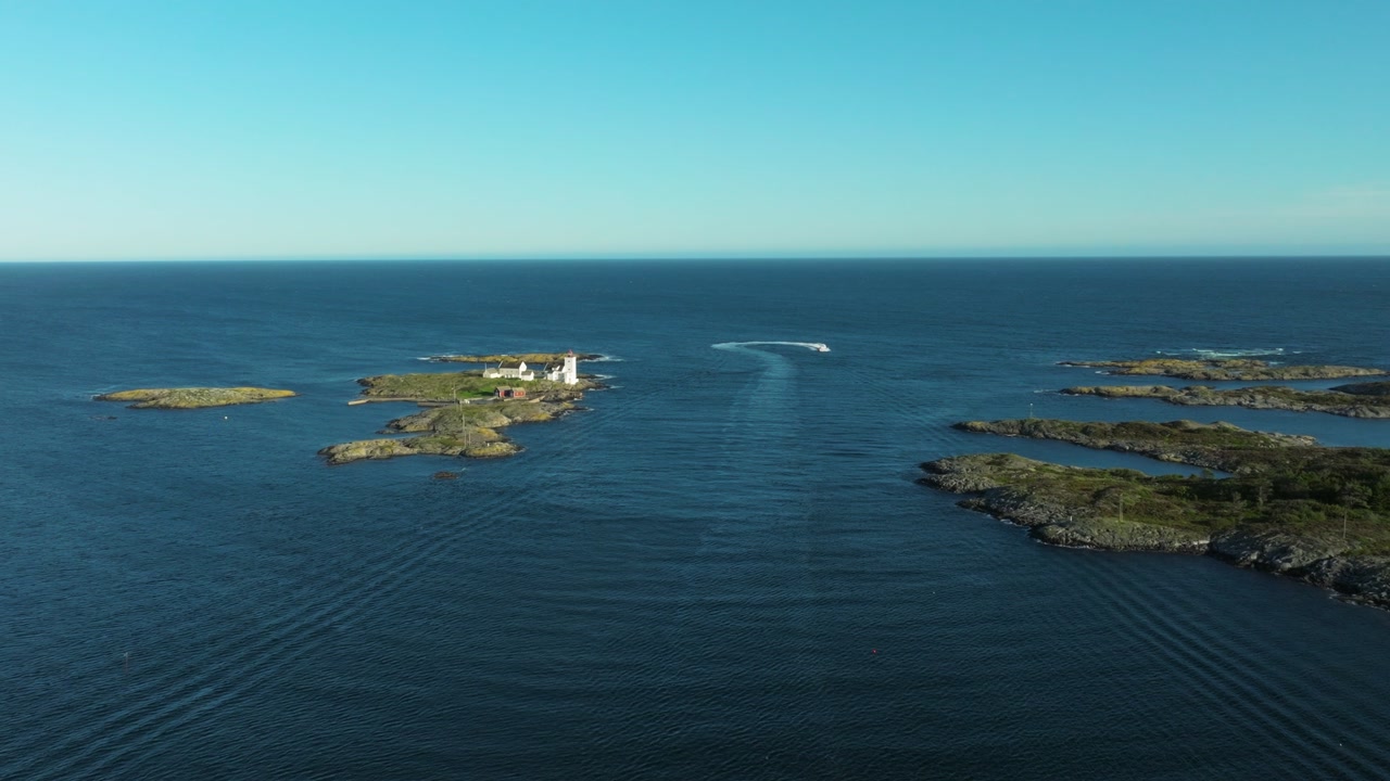 A boat navigates through serene waters, leaving ripples behind as it approaches a small cluster of islands. The sky is clear and bright, enhancing the peaceful atmosphere.