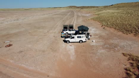 vista aérea cinematográfica sobre autos con carpas en la azotea en una salina en el soleado paisaje del desierto de kalahari en sudáfrica cerca de namibia