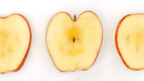 Water-splashes-in-slow-motion.-Top-view:-three-slices-of-a-sweet-apple-washed-by-water-on-a-white-background