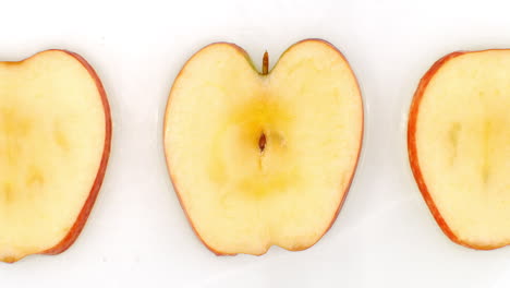 Water splashes in slow motion. Top view: three slices of a sweet apple washed by water on a white background