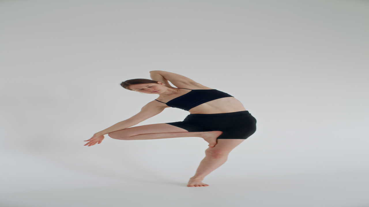 Girl Doing Side Bend in Tree Pose during Yoga Practice in White Studio