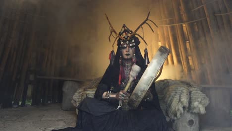 shaman sits inside hut and plays the drum