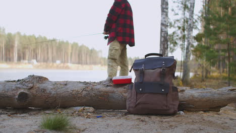 hombre está pescando en el lago de pie en la costa en una mochila de bosque con equipos y cebos en tierrahobby de relajación