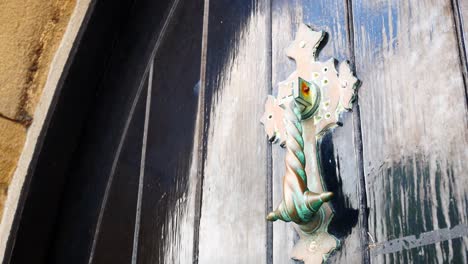 antiguo martinete cruz de cobre verde retorcido en la pesada puerta de madera en piedra arcada medieval dolly izquierda