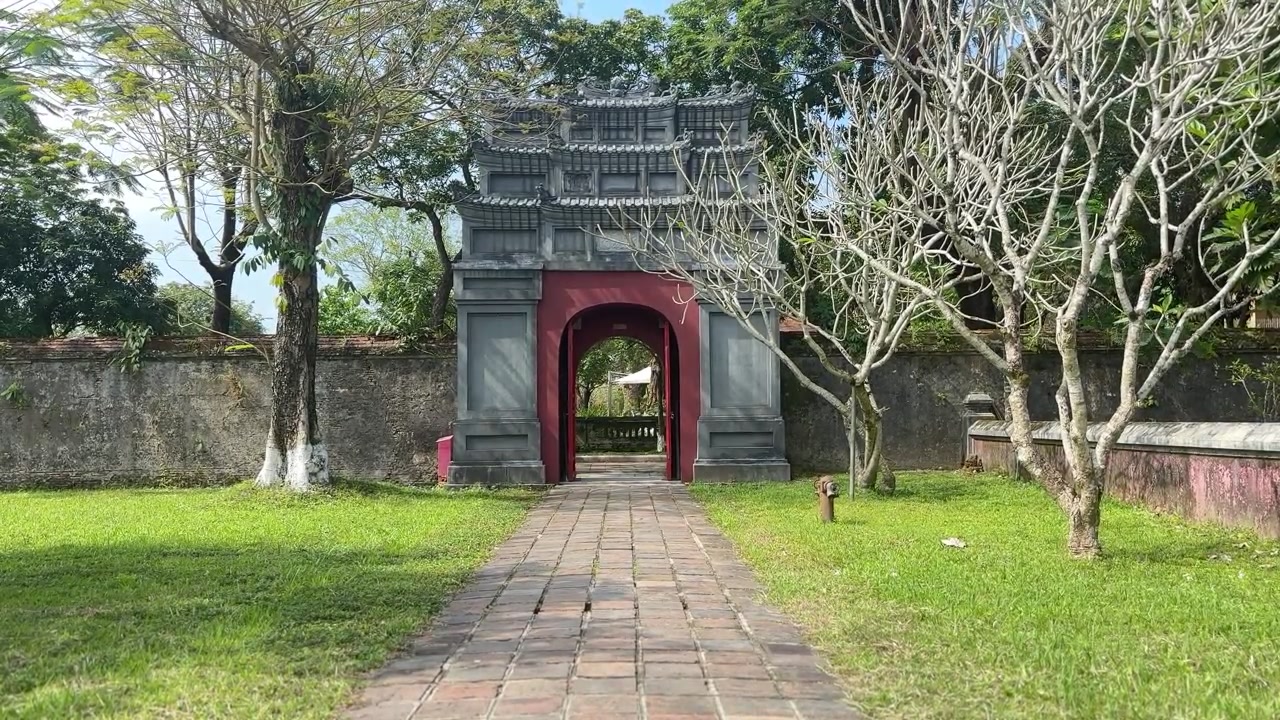 Historisk stenport med rød buegang langs en brolagt sti ved Hue Kejserby. Traditionel vietnamesisk arkitektur omgivet af haver, der fremviser kejserlig arv og kulturturisme
