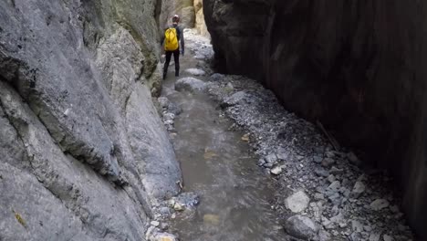 male with yellow pack descends river canyon with flowing water on foot