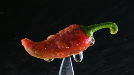 pulverización de agua en pimienta roja pegada en un cuchillo afilado sobre fondo negro, ingredientes picantes
