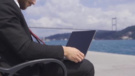 Businessman-working-on-his-laptop-by-the-sea-in-the-city.-Slow-motion.