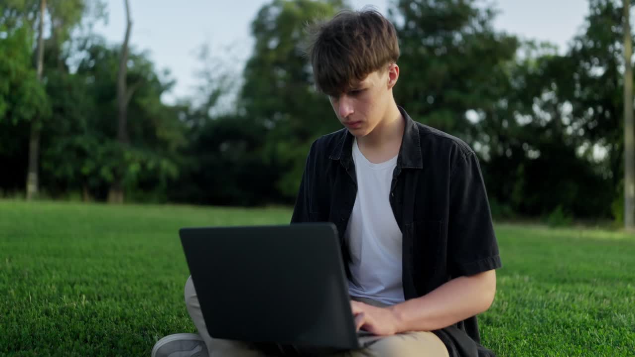 공원에서 노트북을 쓰고 있는 젊은 남자