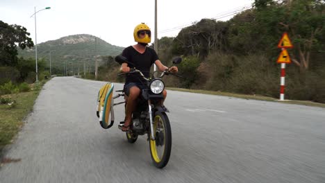 kitesurfer with surfboard rides motorbike to go kiting, exploring vietnam coast