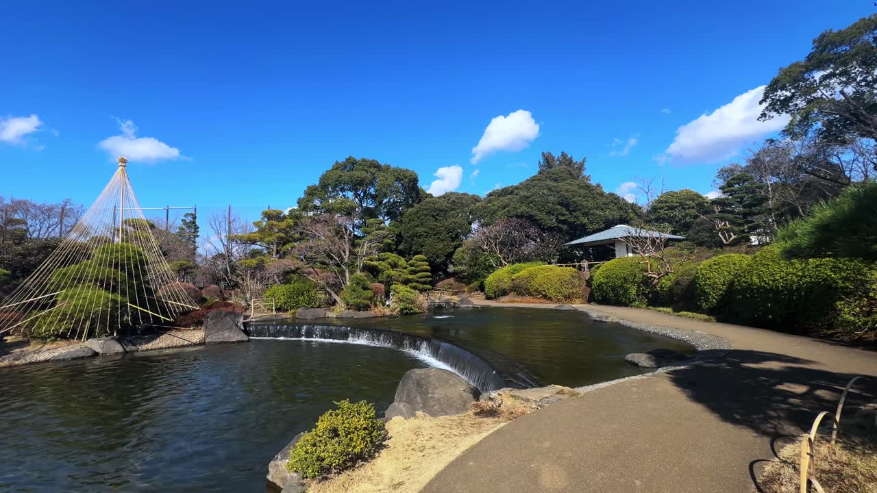 A peaceful Japanese garden with a pond, lush greenery, and a distant house