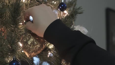 Gorgeous-close-up-shot-of-a-golden,-heart-shaped-ornament-being-hung-on-a-beautiful-lit-up-Christmas