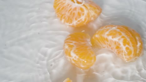 close up peeled mandarin orange falls into water breaks up into slices, white background