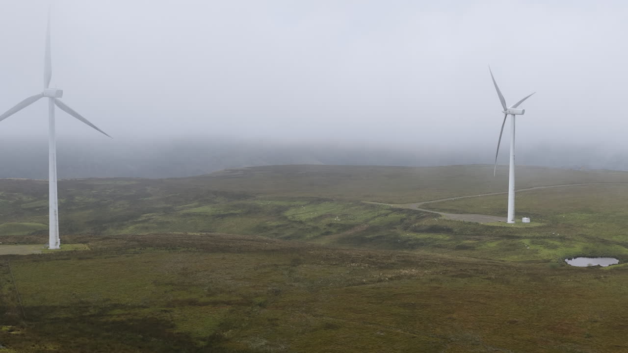 Wide drone shot of wind turbines in West Yorkshire on a grey, misty and cold morning overlooking hills and fields