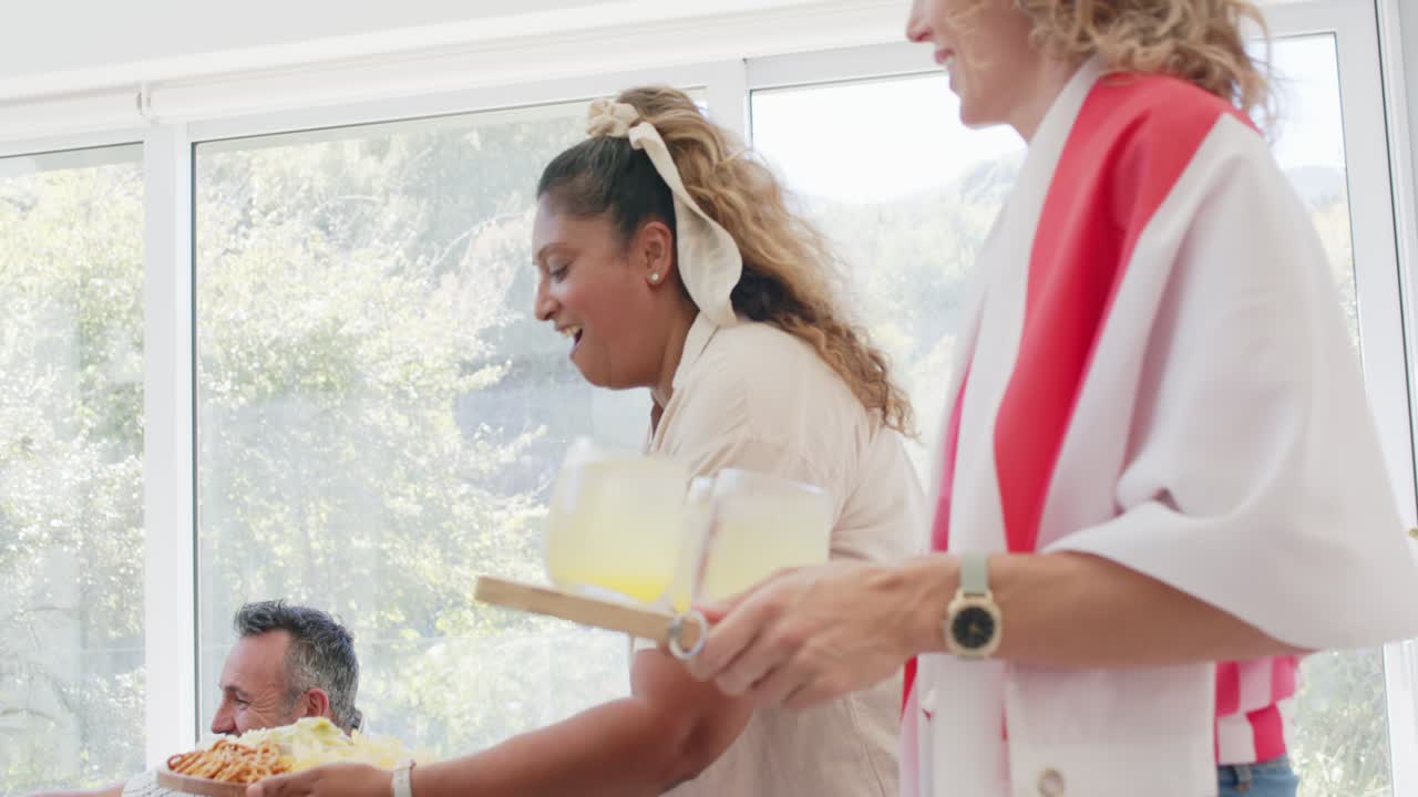 Diverse friends reacting to off-frame event, women bringing pizza and tray with glasses to table