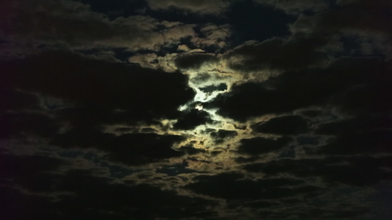 Aerial view in front of the full moon in middle of clouds, dark, moody evening