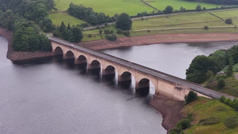 aerial footage smoothly pans across a historic arched bridge spanning ladybower reservoir, surrounded by lush countryside and forest under soft daylight