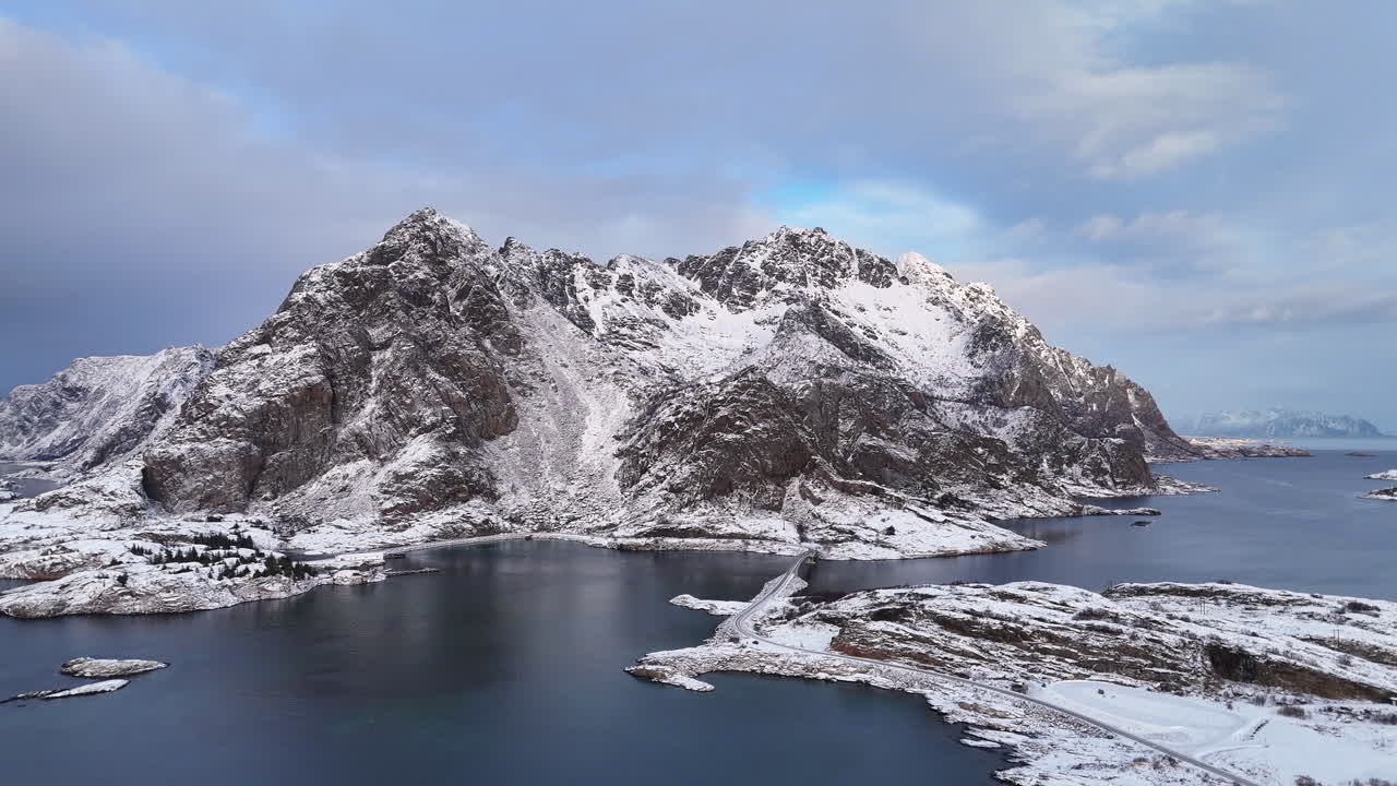 Cinematic aerial view of Henningsvær, a charming fishing village in Lofoten, Norway, surrounded by snowy mountains, Arctic waters, colorful houses, and iconic coastal scenery in winter