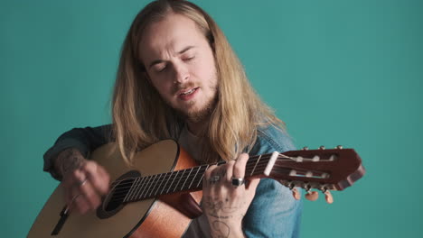 un joven caucásico tocando la guitarra y cantando ante la cámara.