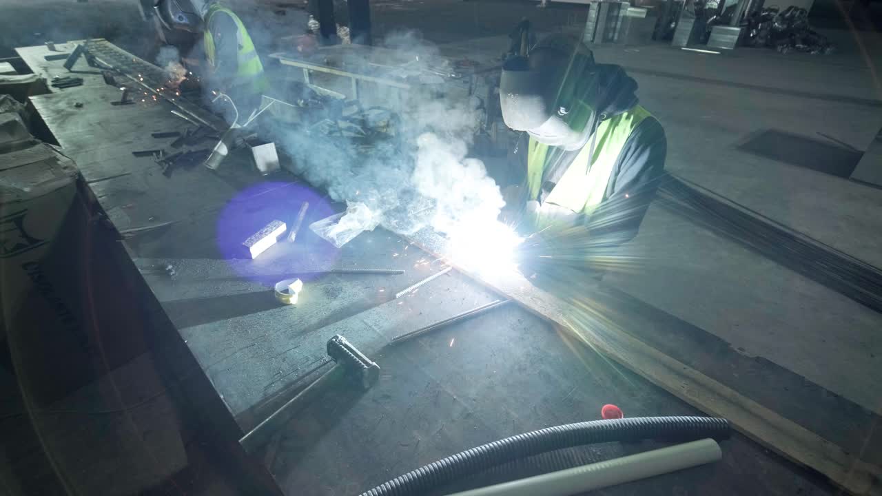 Professional welders are working in the factory wearing safety equipment. Metalwork manufacturing, industrial process.