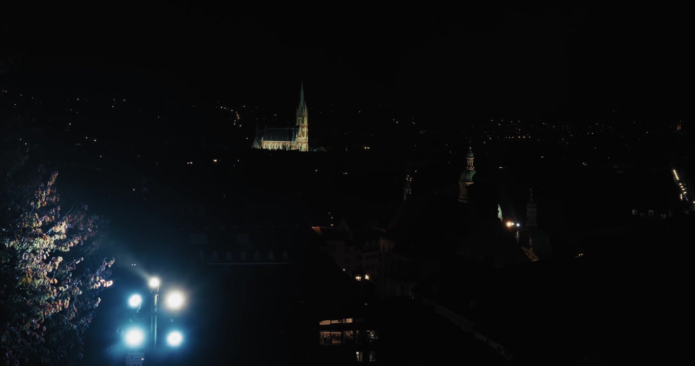Vista notturna di Graz con l'Uhrturm illuminata e un campanile di chiesa brillantemente illuminato in lontananza