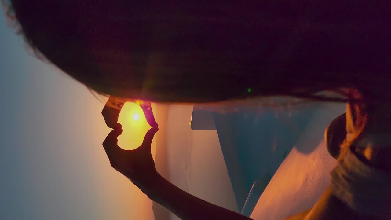 한 여성이 손가락으로 심장을 만드는 해가 지는 모습을 어깨에서 볼 수 있습니다.