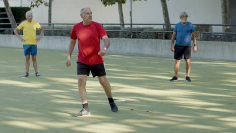 long shot of a focused senior man kicking ball while playing football outdoors with friends