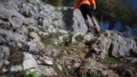 Footage-of-a-person-wearing-shorts,-an-orange-jersey,-a-backpack-and-red-sneakers-while-hiking-up-a-rocky-terrain