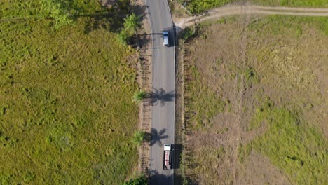 drone aerial point of view tracking an suv car driving on a countryside road with large green rural areas and farming landscapes, costa rica