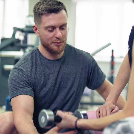 fitness, sport, exercising and weightlifting concept - young woman and personal trainer with dumbbells flexing muscles in gym