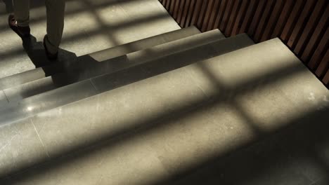 slow motion shot of a man walking down sunlit stairs casting elongated shadow on steps