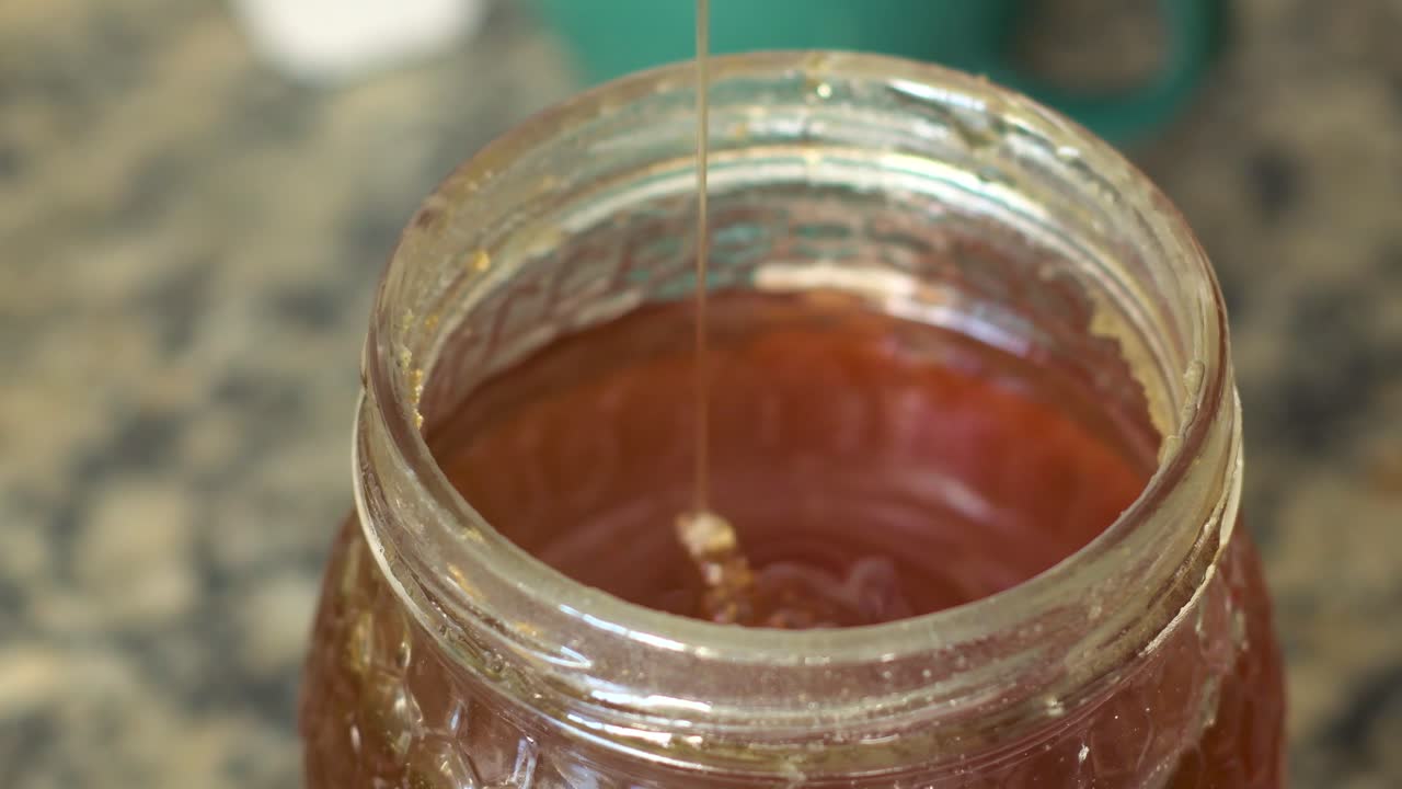 Close up view of a spoon taking honey from a jar