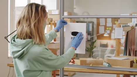 woman posting a "please wear a mask" sign at a store or office