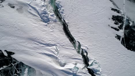 aerial above the deep crack on snow covered frozen ice surface of lake baikal. natural landmark. winter landscape. popular touristic destination. top down view.