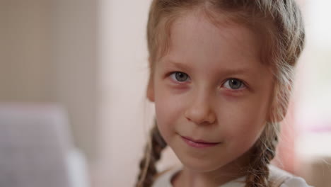 una niña bonita con trenzas hace un guiño a la cámara en casa