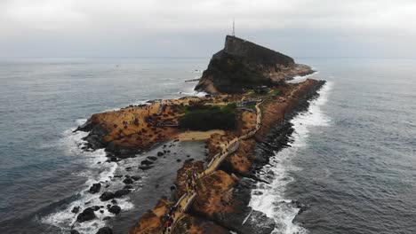 people on the walkways exploring the yehliu geopark, the tourist attraction yehliu cape on the sea in drone aerial 4k shot. wanli district, new taipei, taiwan.