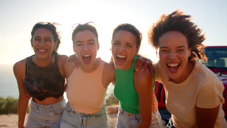 Portrait-Of-Laughing-Female-Friends-Standing-By-Open-Top-Car-On-Road-Trip